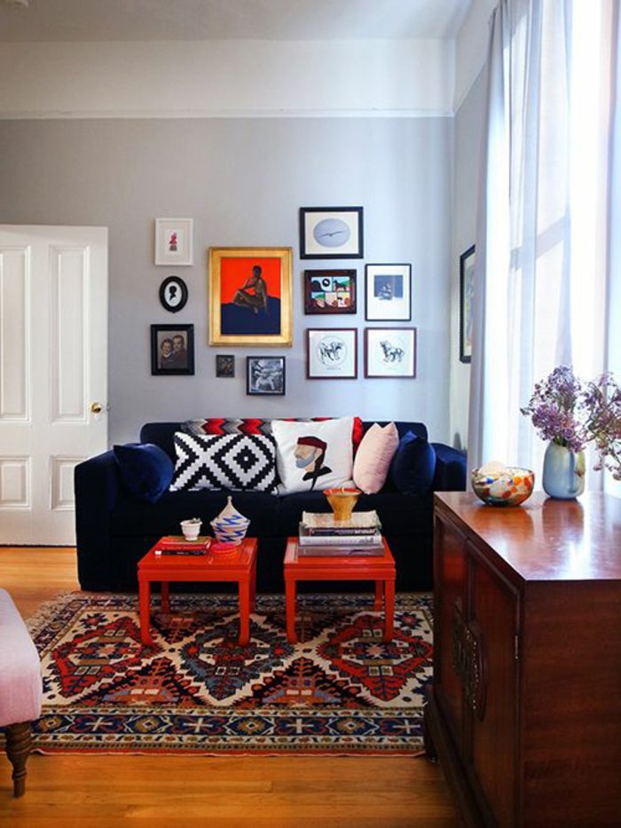 graues Zimmer mit viele Wandbilder, bunte Kissen, blaues Sofa, Regal aus Holz