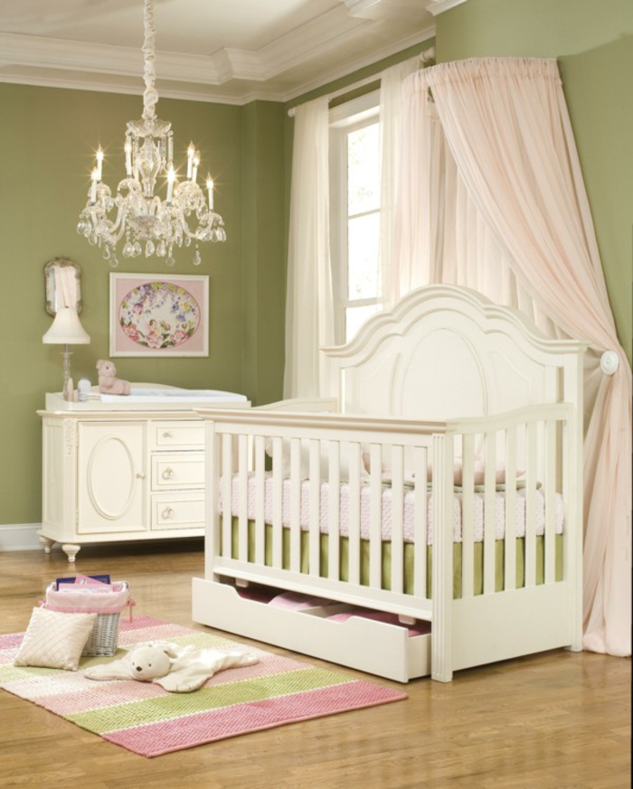 stilvolles Babyzimmer, grüne Wände, weiße Holzmöbel, verspielter Kronleuchter, Babybett mit hellrosa Himmel