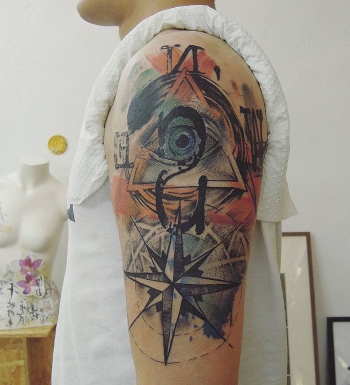 ein mann mit einem verrückten bunten tattoo auf dem schulter mit einem großen blauen auge und einem großen schwarzen kompass