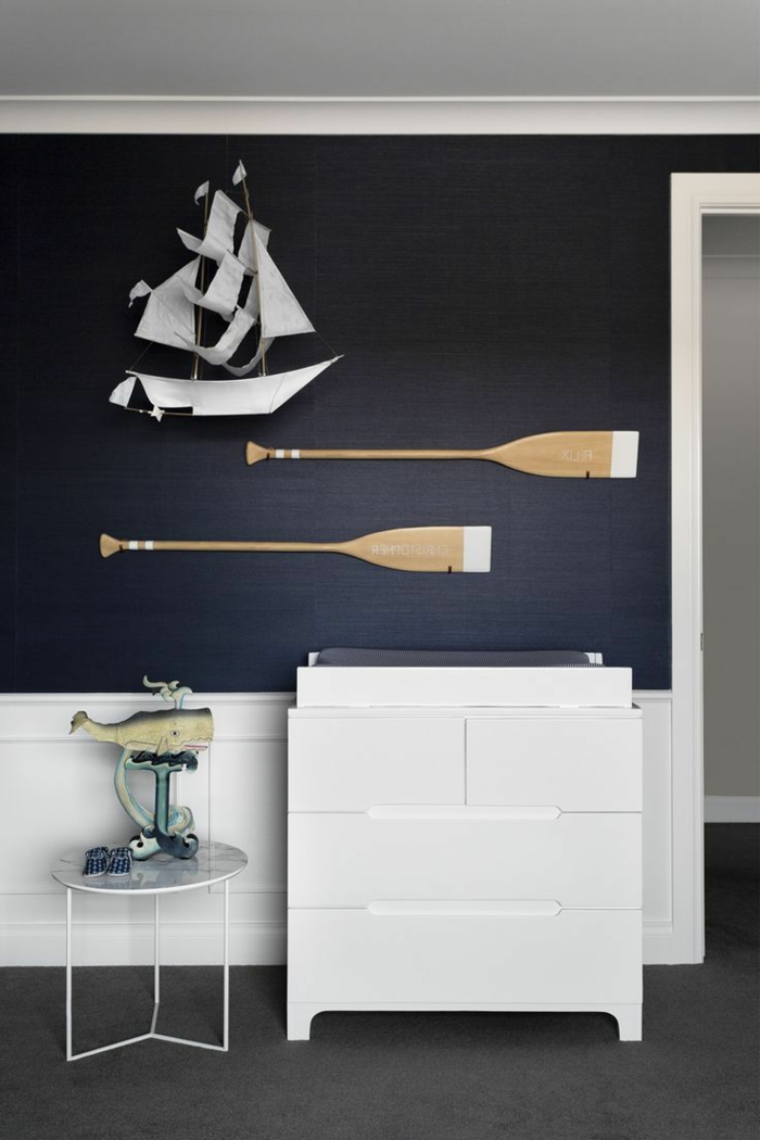 Dunkelblaue Wand mit aufgehängtes Segelboot und zwei Ruder, weiße Kommode, maritime Farben und deko Figuren