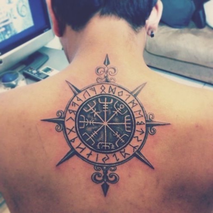 hier ist ein mann mit einem großen, schwarzen, modernen tattoo mit einem schwarzen kompass auf dem rücken und ohrringen