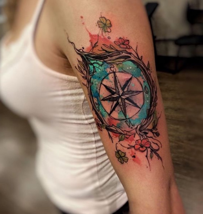 hier finden sie eine junge frau mit einer märchenhaften, großen und schönen tattoo mit einem schwarzen, großen kompass mit zwei roten blumen und zwei grünen blumen