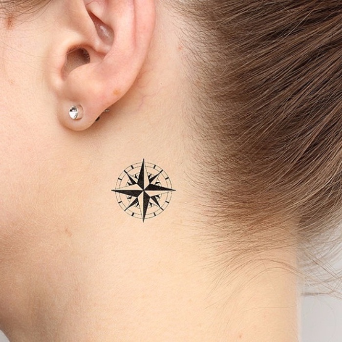 compass tattoo - eine junge frau mit tattoo mit einem schwarzen kleinen mini kompass und ohrringen