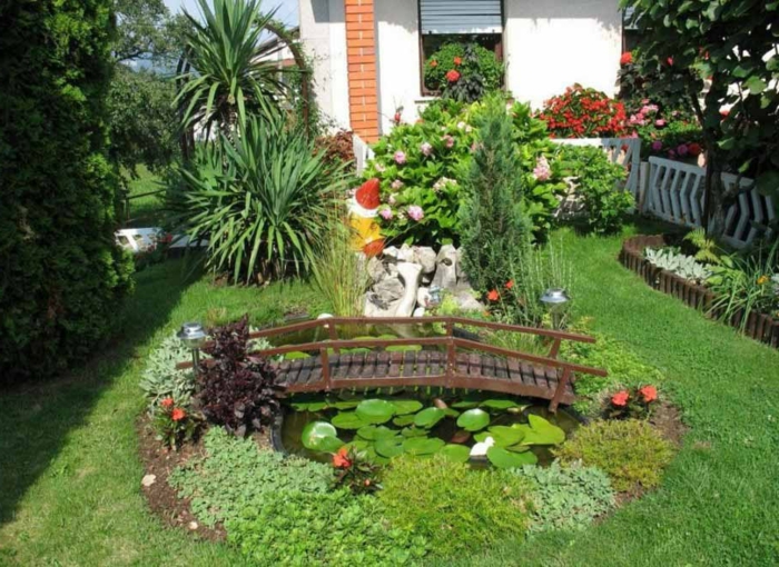 ein minimalistischer Garten mit kleinen Seerosen und viel Grün Teich mit Brücke