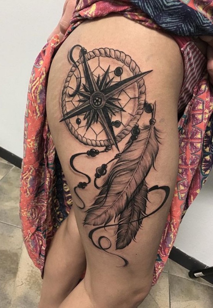 eine große tätowierung mit einem großen schwarzen kompass mit schwarzen pfeilen und zwei langen weißen federn - idee für einen tattoo für frau
