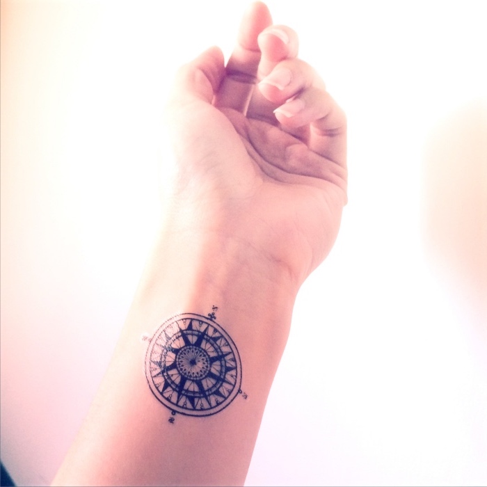 ein kleiner schwarzer tattoo mit einem schwarzen kompass auf dem handgelenk
