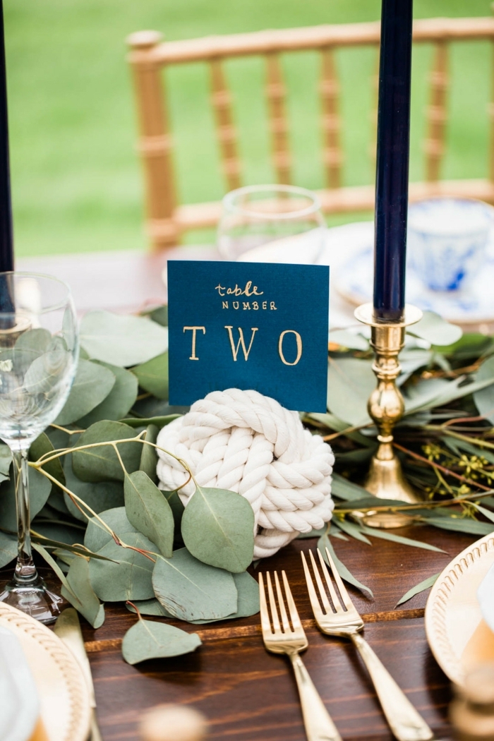 Maritime Tischdeko Hochzeit, Holztisch dekoriert mit grünen Blättern, weißer Knotenball, große blaue Kerze