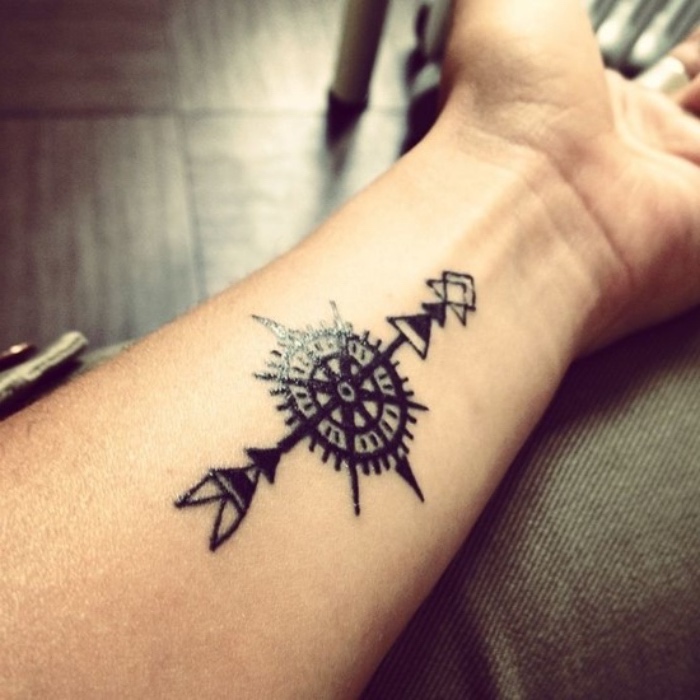 compass tattoo - eine hand mit einem schwarzen tattoo mit einem schwarzen langen pfeil und einem kleinen schwarzen kompass - tattoo auf dem handgelenk