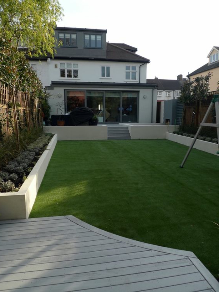 ein künstlicher Gras Rasen, Bäume an den Zaun, Haus im minimalistischem Stil - Gartengestaltung Beispiele