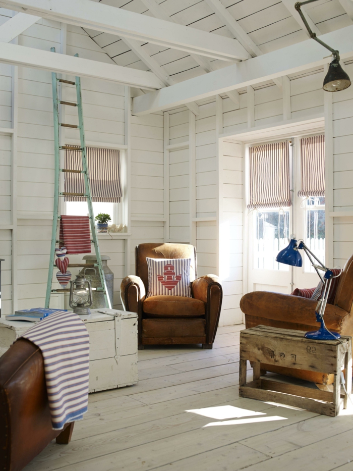 Wohnzimmer maritimer Stil mit Dachschrägen, drei Sessel aus Leder, weiß blaue Kissen mit Anker Bild, blaue Lampe, 