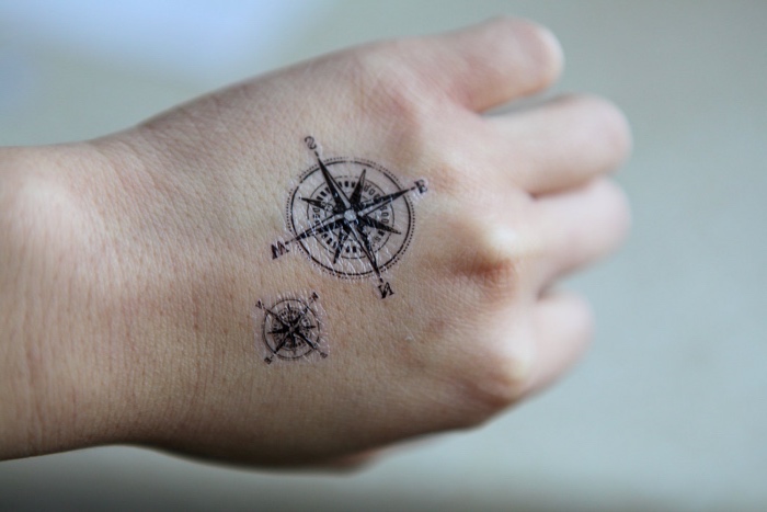 zwei schöne kleine compass tattoos mit schwarzen kompassen auf der hand