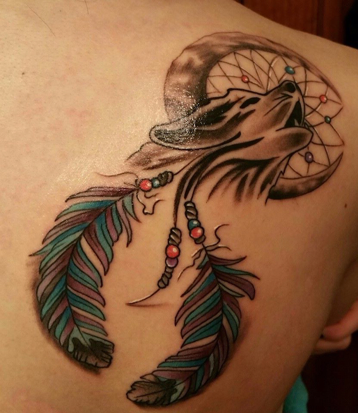 das ist eine tolle idee für tattoo traumfänger mit einem schwarzen heulenden wolf mit einem mond und zwei blauen federn - tätowierung auf dem schulterblatt einer jungen frau