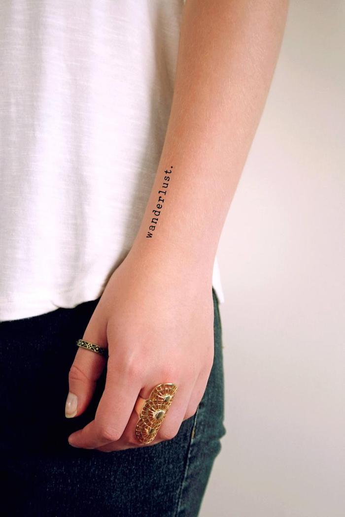 Kleines Tattoo am Unterarm im Schreibmaschinenstil, Wanderlust Tattoo, goldene Ringe, weißes Top und Jeans 