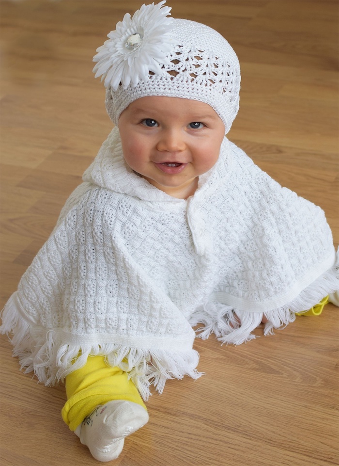 ein niedliches kleines Mädchen mit weißem Poncho, wie Sie für Baby Poncho stricken