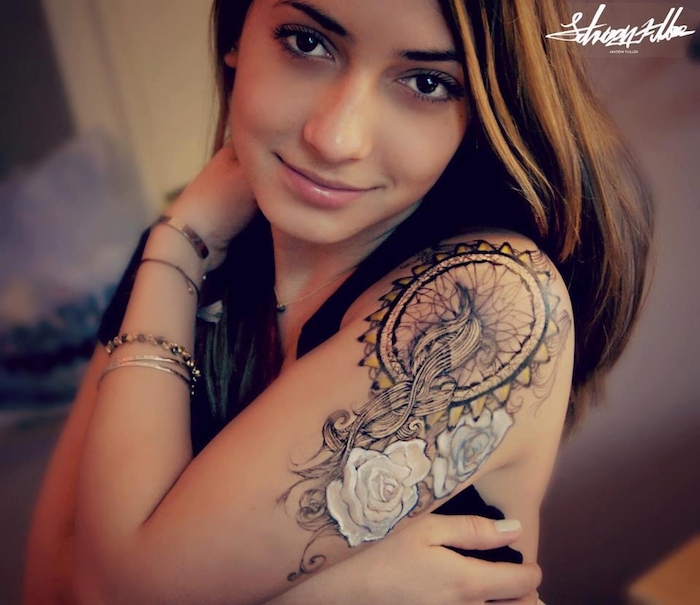 hier ist eine junge frau mit einem großen tattoo mit einem traumfänger mit zwei weißen großen rosen auf dem schulter