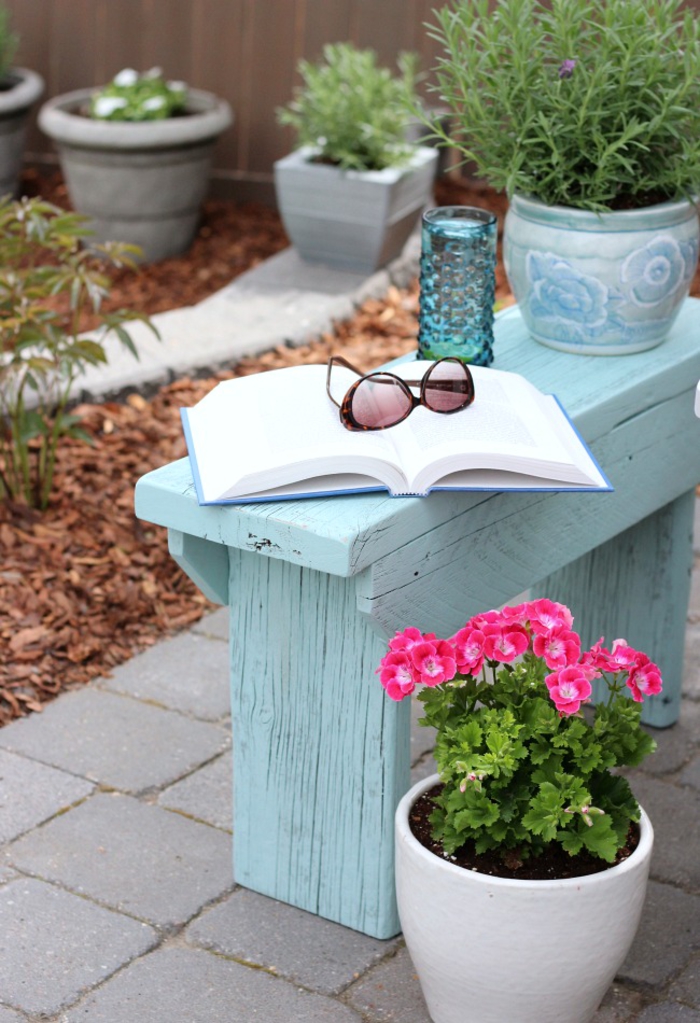 Garten im Landhausstil, blaue Holzbank, Blumentöpfe, geöffnetes Buch, Sonnenbrille darauf
