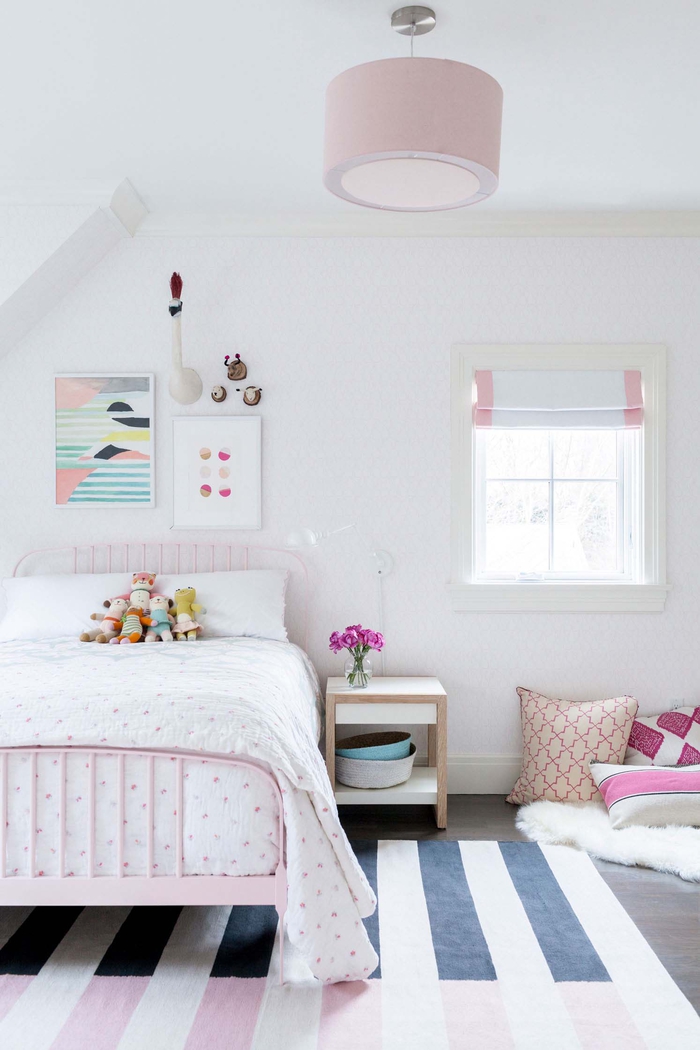 Kinderzimmer in Pastelltönen, rosa Bett, kleine Kuscheltiere darauf, Dekokissen auf dem Boden, Blumenstrauss auf dem Nachttisch