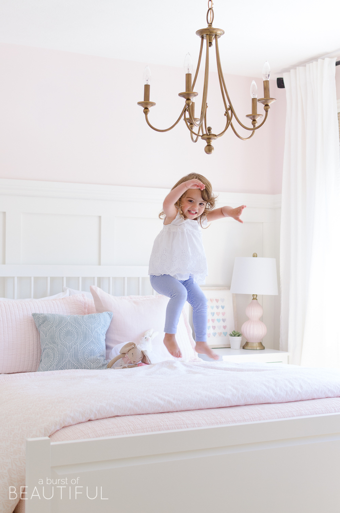 Schlafzimmer in Rosa, weißes Holzbett, verspielter Kronleuchter, süßes Kind springt auf dem Bett