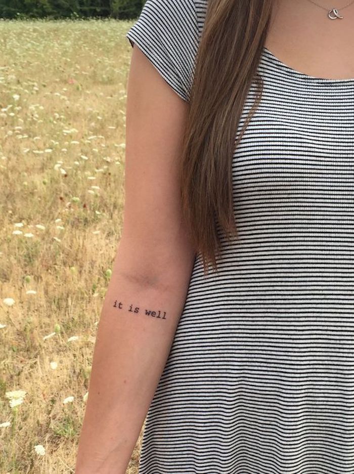 Schrift Tattoo es geht mir gut auf dem Arm ein graues Kleid auf Streifen auf einer Wiese