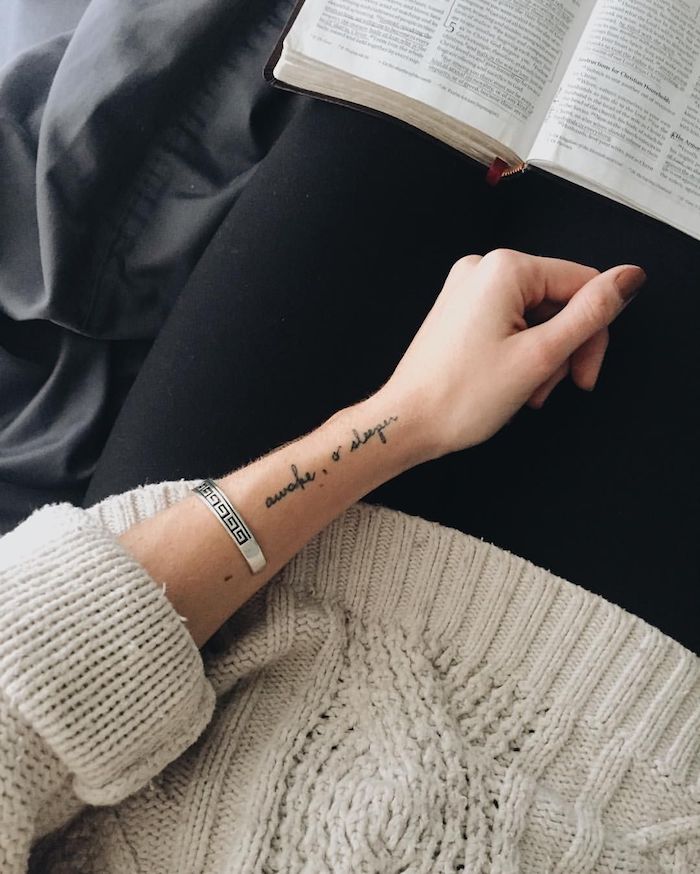 Tattoo in feiner Schreibschrift am Handgelenk, Frauen Tattoos, lässiges Outfit, weißer Pulli und schwarze Hose, silbernes Armband 