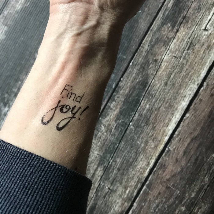 Mittelgroßes Tattoo am Handgelenk in Schreibschrift und Schreibmaschinenstil, Find Joy Tattoo 