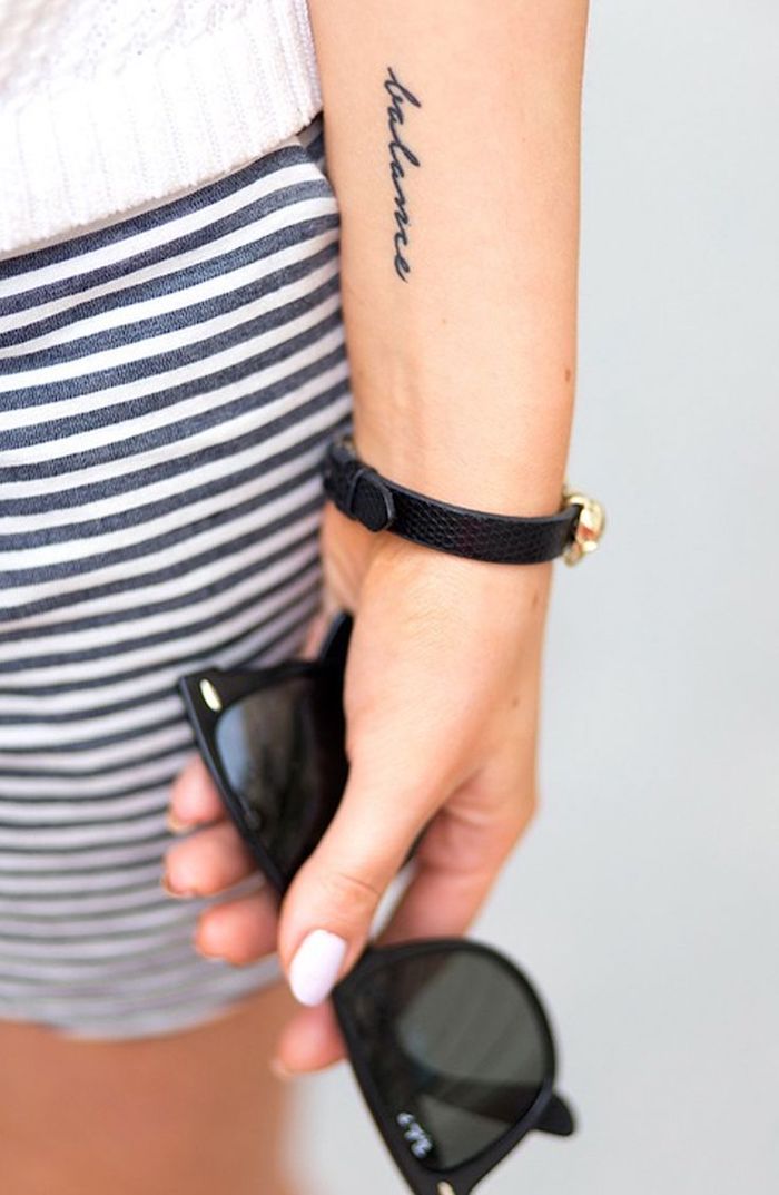 Kleines Unterarm Tattoo in Schreibschrift, gestreifter Rock und weißes Top, weißer Nagellack, Sonnenbrille in der Hand