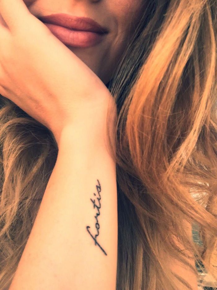 Kleines Tattoo am Unterarm in Schreibschrift, braune gewellte lange Haare, matter Lippenstift 