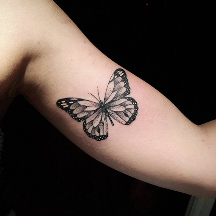 eine hand mit einem schwarzen tattoo butterfly - hier ist ein fliegender schwarzer schmetterling mit großen schwarzen flügeln 