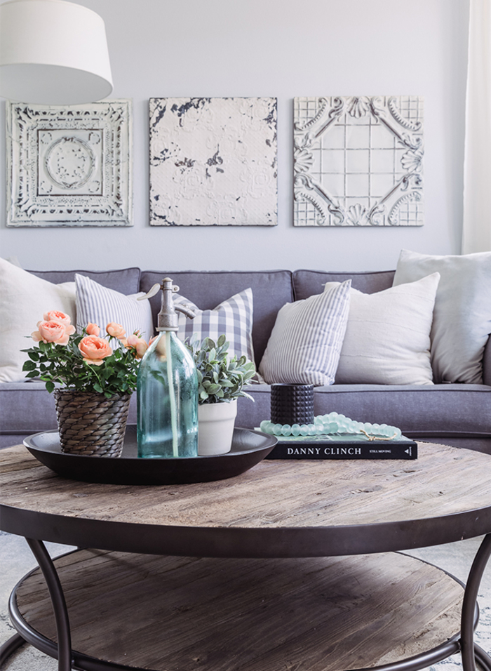 graues Sofa, helle Dekokissen, Holztisch, Blumentöpfe, Buch und Perlen, in hellen Pastelltönen einrichten