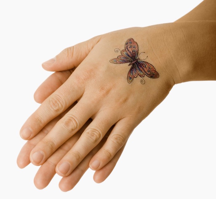 hier sind zwei hände und ein bunter, kleiner fliegender schmetterling mit bunten flügeln - idee für einen wirjlich tollen butterfly tattoo