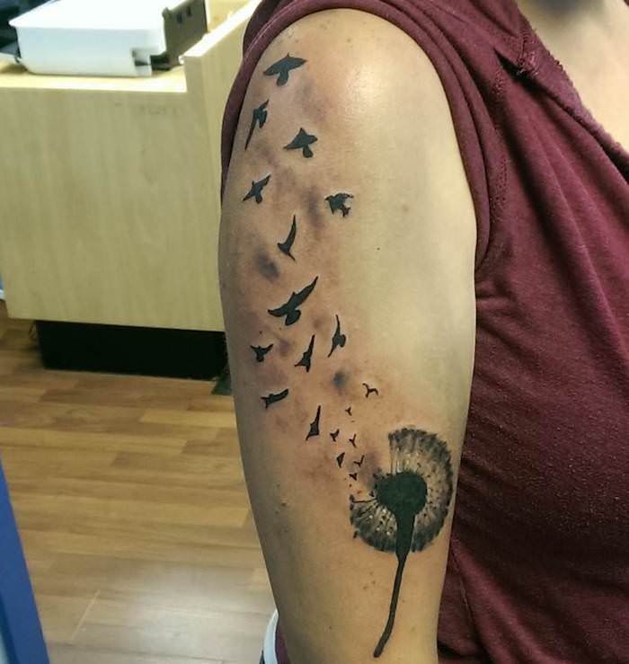 tattoo vogel, schwarz-graue tätowierung mit blume und fliegenden vögeln am oberarm