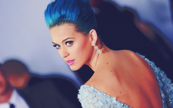 Katy Perry mit blauen Haaren, Abendkleid mit nacktem Rücken, violette Lippen. auffällige Ohrringe