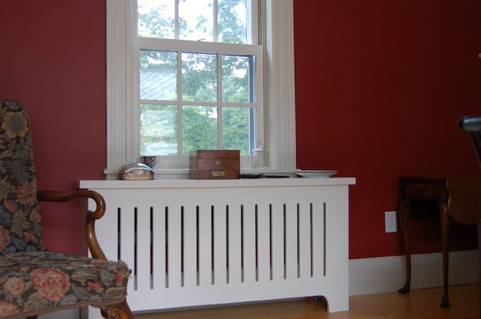weiße Heizungsverkleidung im Kontrast mit den roten Wänden, bunter Sessel