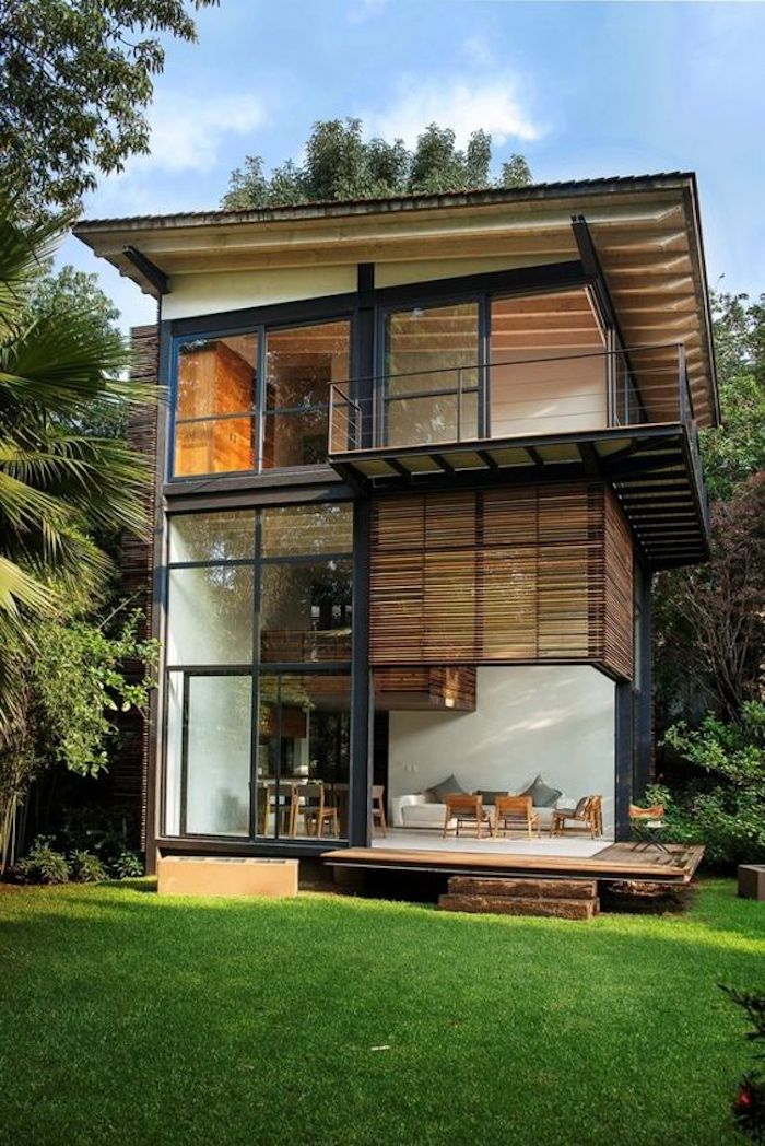 schönes zweistöckiges landhaus aus containern - mit einer terrasse, stühlen, tisch und einem garten mit palmen und grass
