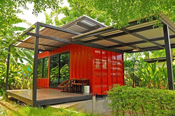 werfen sie einen blick auf diese idee für ein container haus - hier ist ein kleines rotes landhaus mit terrasse und sofas und einem garten mit grünen pflanzen und bäumen