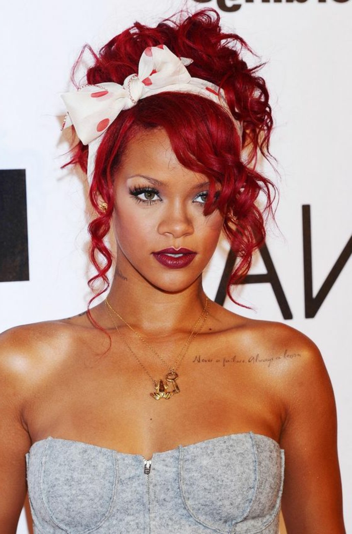 Rihanna mit knallroten Haaren, weißer Haarband mit roten Punkten, goldene Ketten, grauer Top