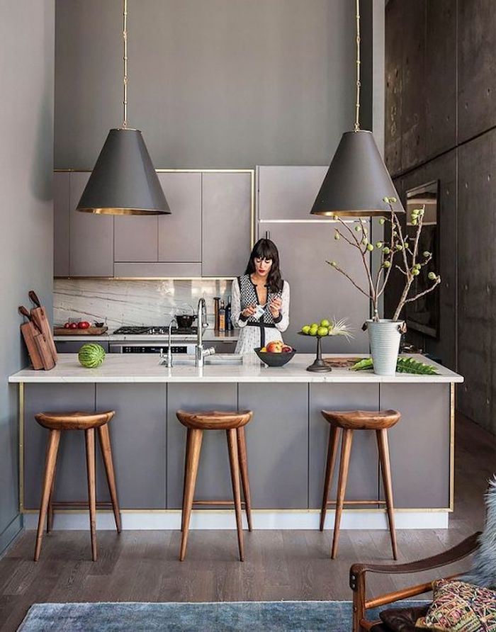 offene Küche in grauer Farbe mit zwei ausgefallenen Lampenschirmen, eine Frau bereitet den Nachtisch
