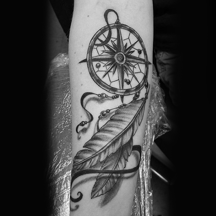 unterarm tattoo in schwarz und grau, traumfänger mit kompass und federn