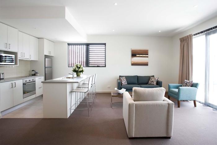 Offene Küche mit Wohnzimmer - weiße Küche und bunte Sessel, beige Vorhänge