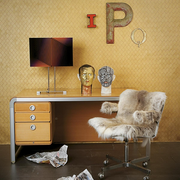 Arbeitszimmer mit Vintage Einrichtung, Schreibtisch aus Holz, Stuhl, bedeckt mit Pelz, Zeitungsblätter am Boden, zwei Skulpturen auf dem Tisch