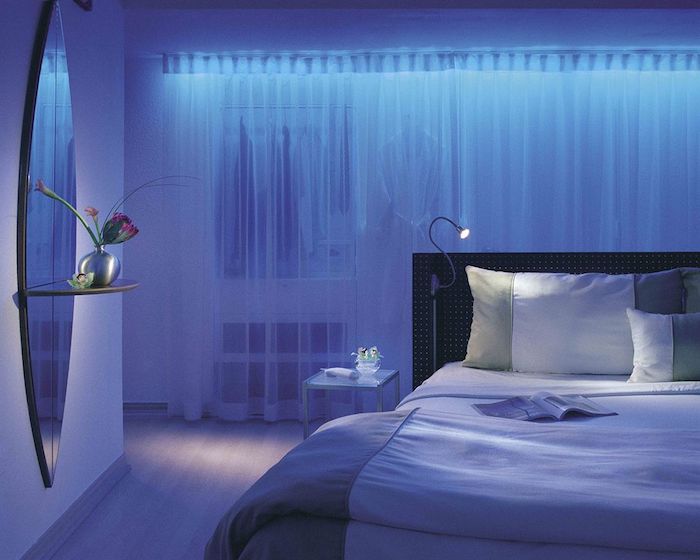 blaues Schlafzimmer mit indirekter Beleuchtung, weiße halbdurchsichtige Vorhänge