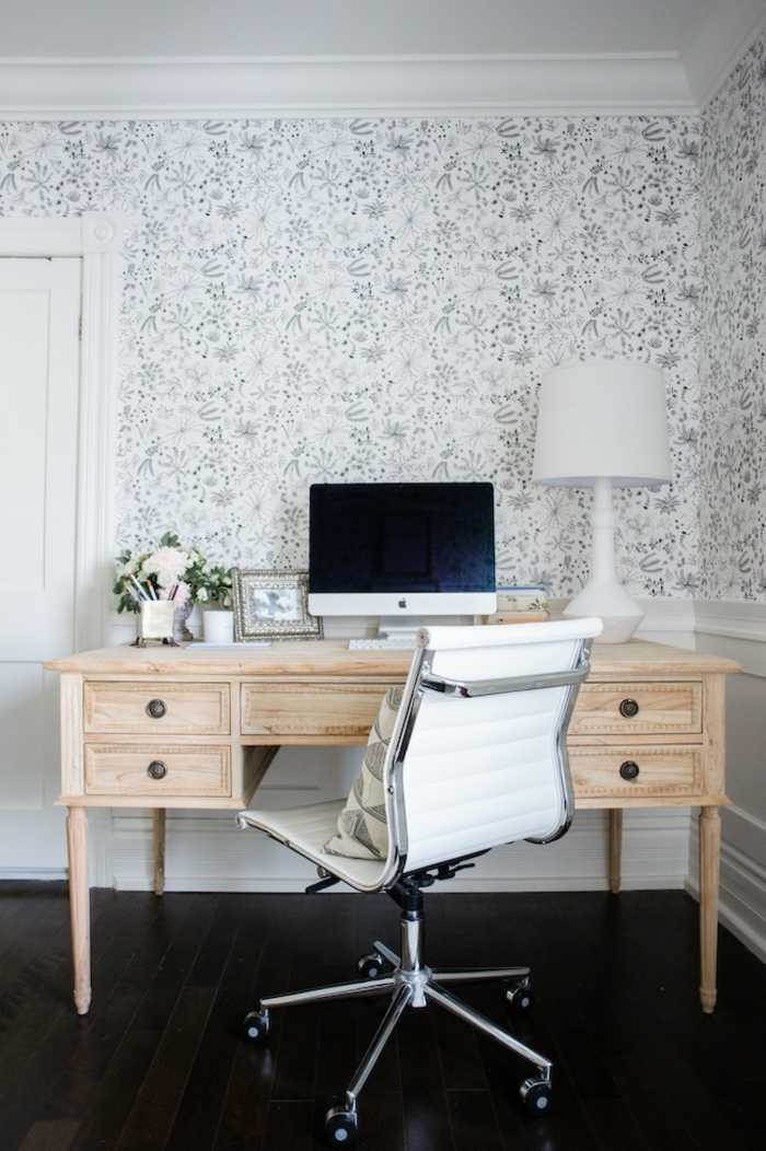 Schreibtisch aus Massivholz, Stuhl mit Rollen, weiße Nachttischlampe, weiße Tapeten mit Blumenmustern