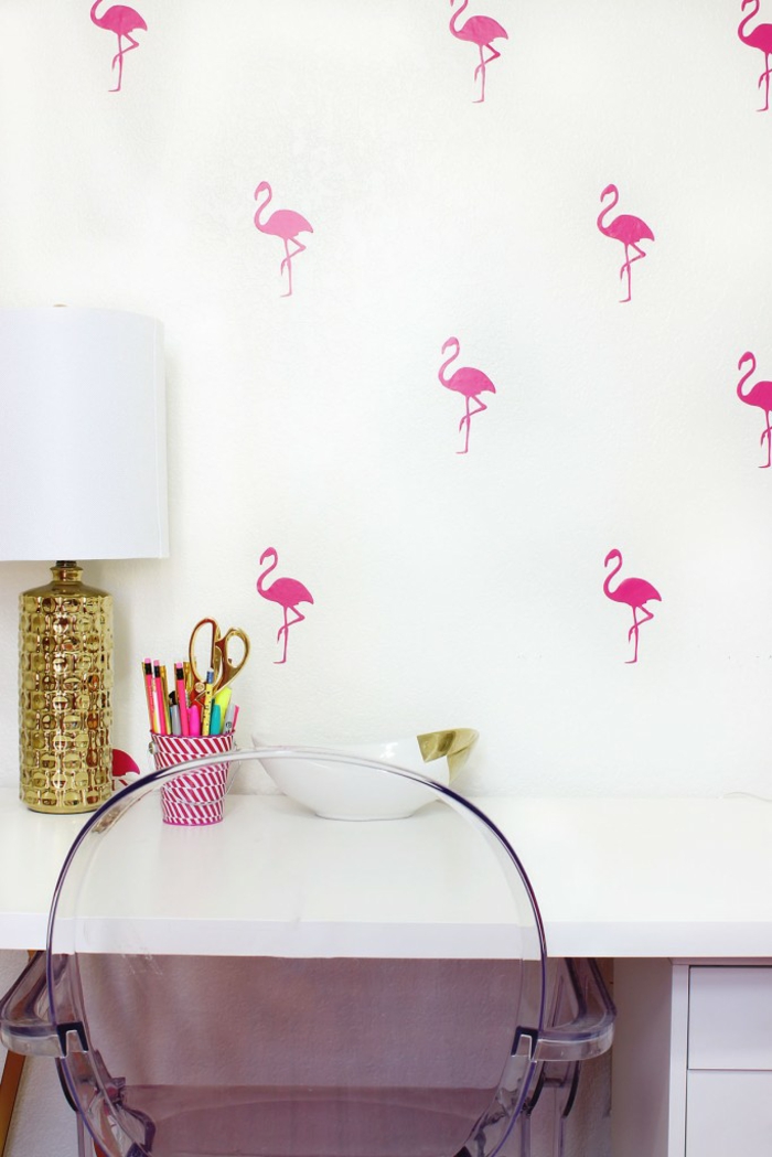 Arbeitszimmer einrichten, weiße Wand mit kleinen Flamingos, Holz-Schreibtisch, durchsichtiger Kunststoffstuhl, Vintage Nachttischlampe, Stifthalter