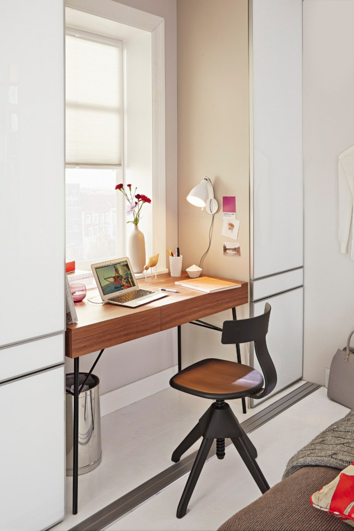 praktische Idee für kleine Räume, Schreibtisch am Fenster, weiße Vase mit Nelken, weiße Nachttischlampe an der Wand, gelbes Heft und Kugelschreiber