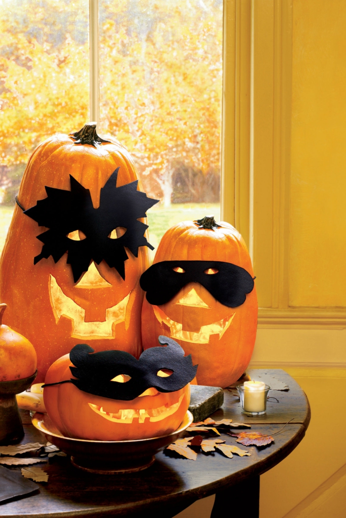 Kürbusse scnitzen, gruselige Kürbisgesichter mit Masken, Halloween Tischdekoration, Herbstblätter und Duftkerzen