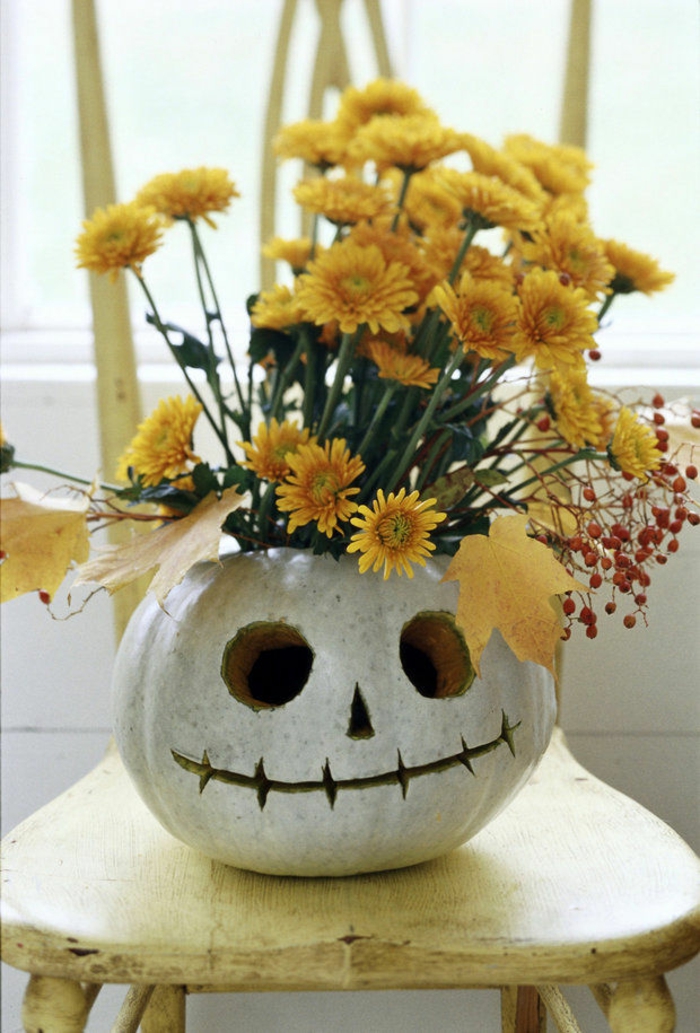 ein weißes Kürbisgesicht mit gelben Blumen und Blätter als Dekoration