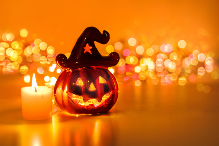 eine Figur aus Glas neben einer Kerze und glänzende Lichter im Hintergrund - Halloween Hintergrund