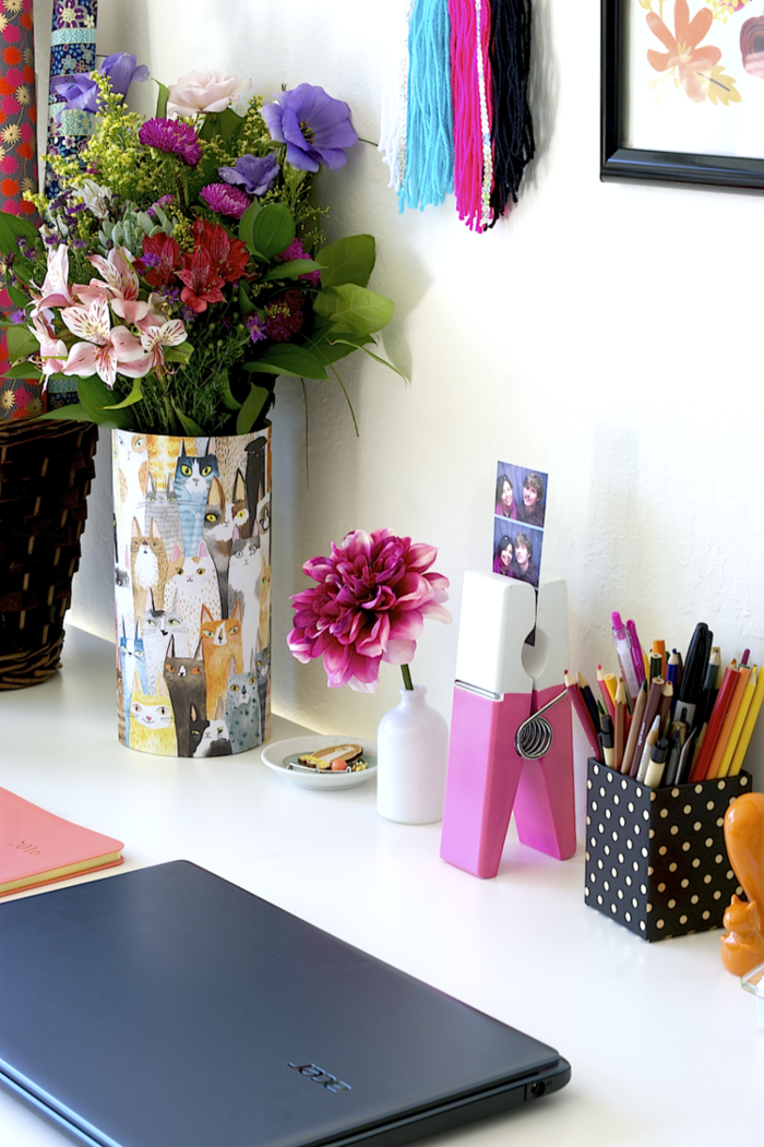 weißer Schreibtisch, Vase mit Katzen, Stifthalter mit vielen Kugelschreibern und Bleistiften, große Chrysantheme, Laptop und Fotohalter 
