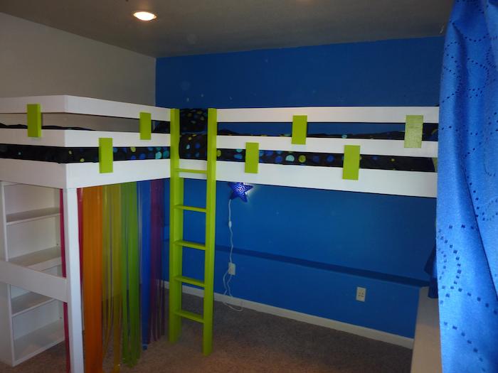 Kinderbett in weißer Farbe mit grünen Akzent, davon hängt eine Gardine in den Farben von Regenbogen