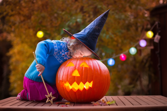 ein kleines Mädchen als Hexe gekleidet spielt mit Kürbisgesicht am Halloween